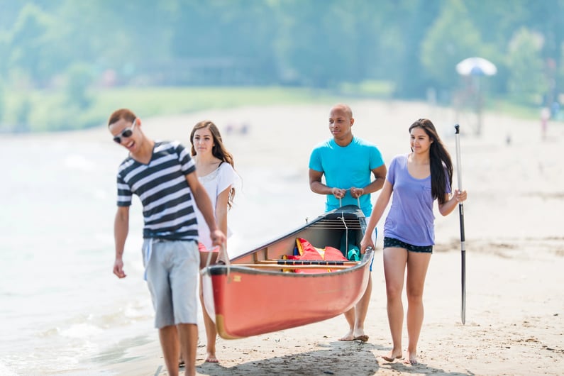 teens carrying a canoe on the beach